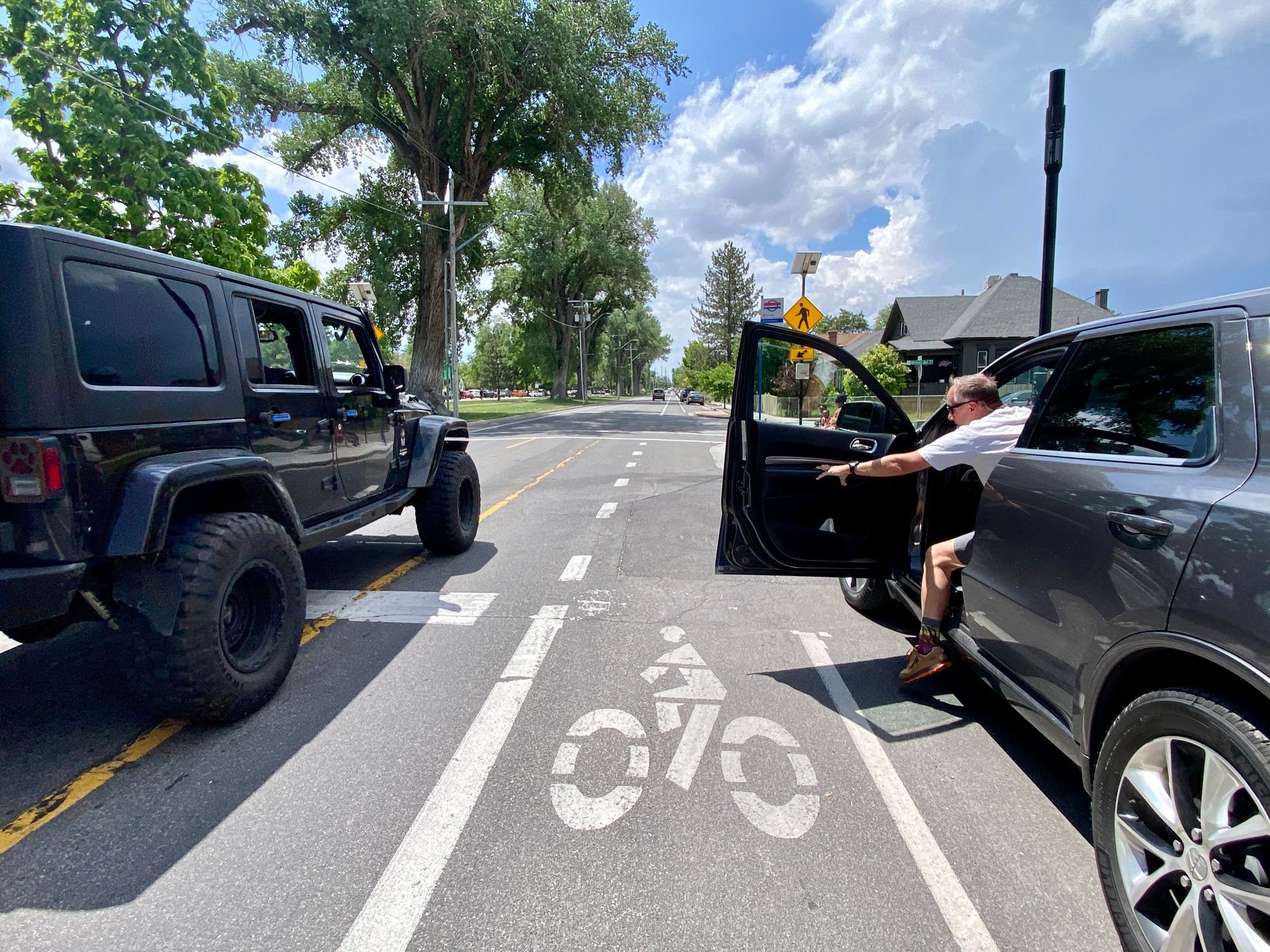 A bicycle lane with cars on either side and a car door opening into a cyclists path