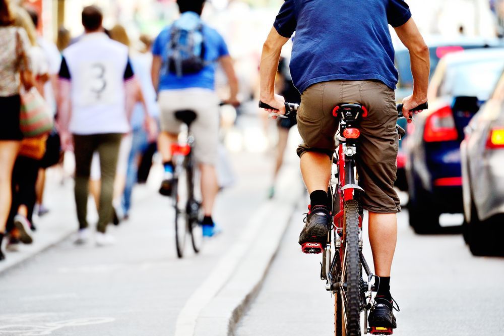 Busy city street filled with cars, pedestrians and bicycles on the road and in bike lanes.