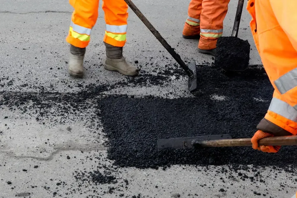 construction work crew repairing defect in road with new asphalt